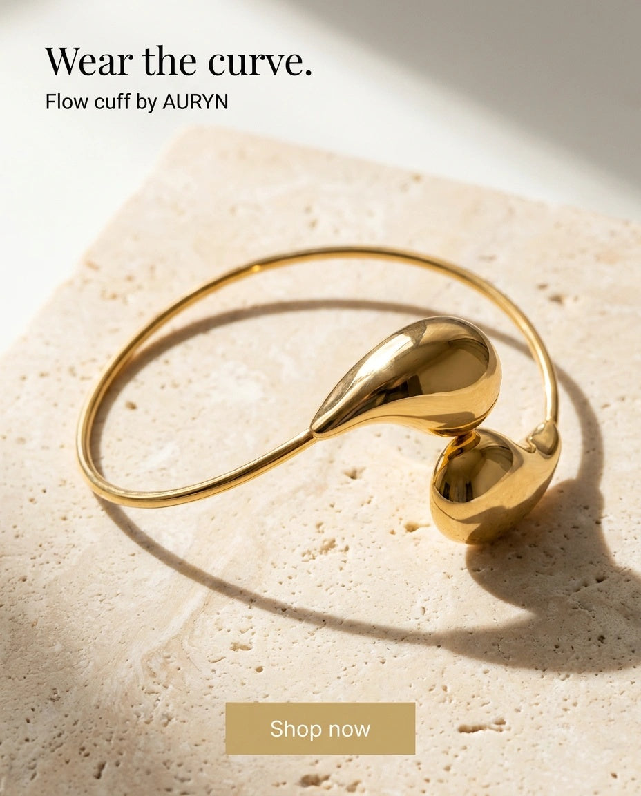 AURYN Flow gold-tone open cuff on pale stone — editorial styling